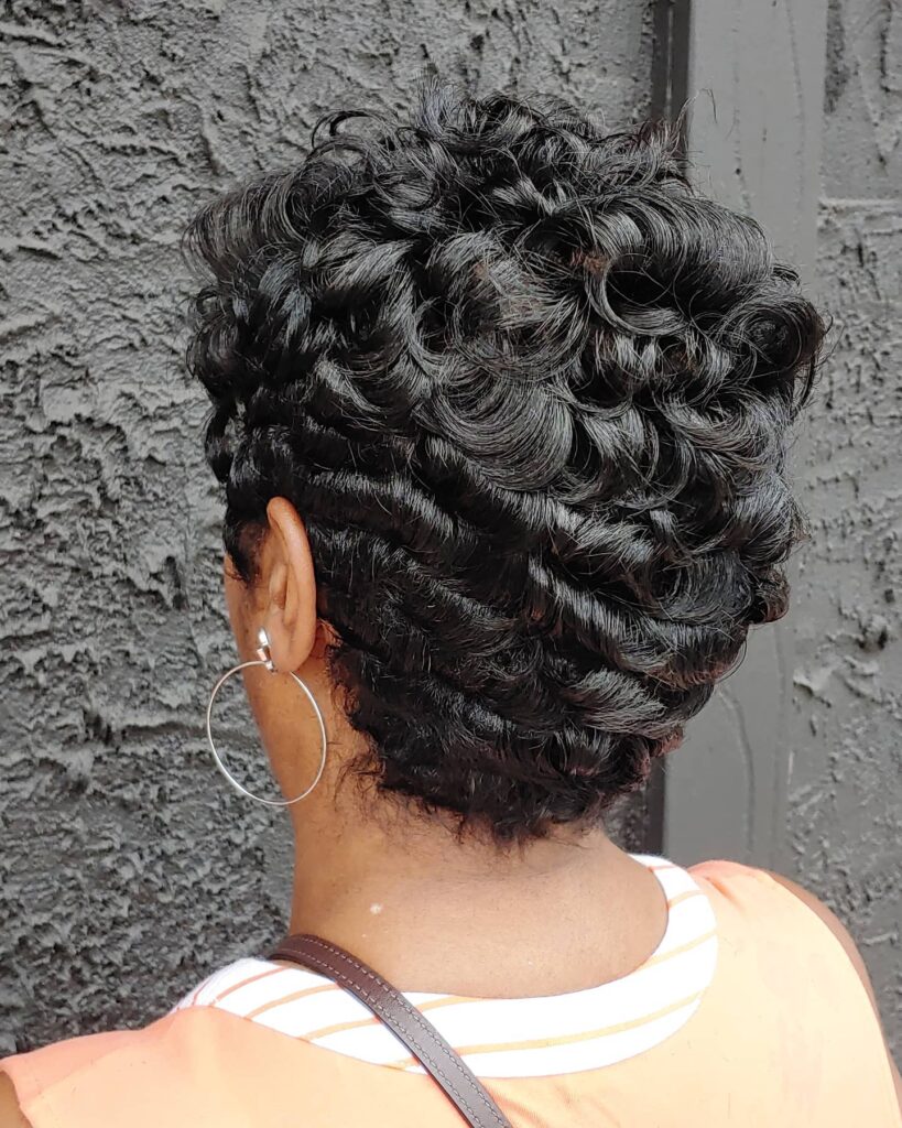 A back view of a woman with short dark hair styled in sleek finger waves on the bottom and voluminous tight curls on top.