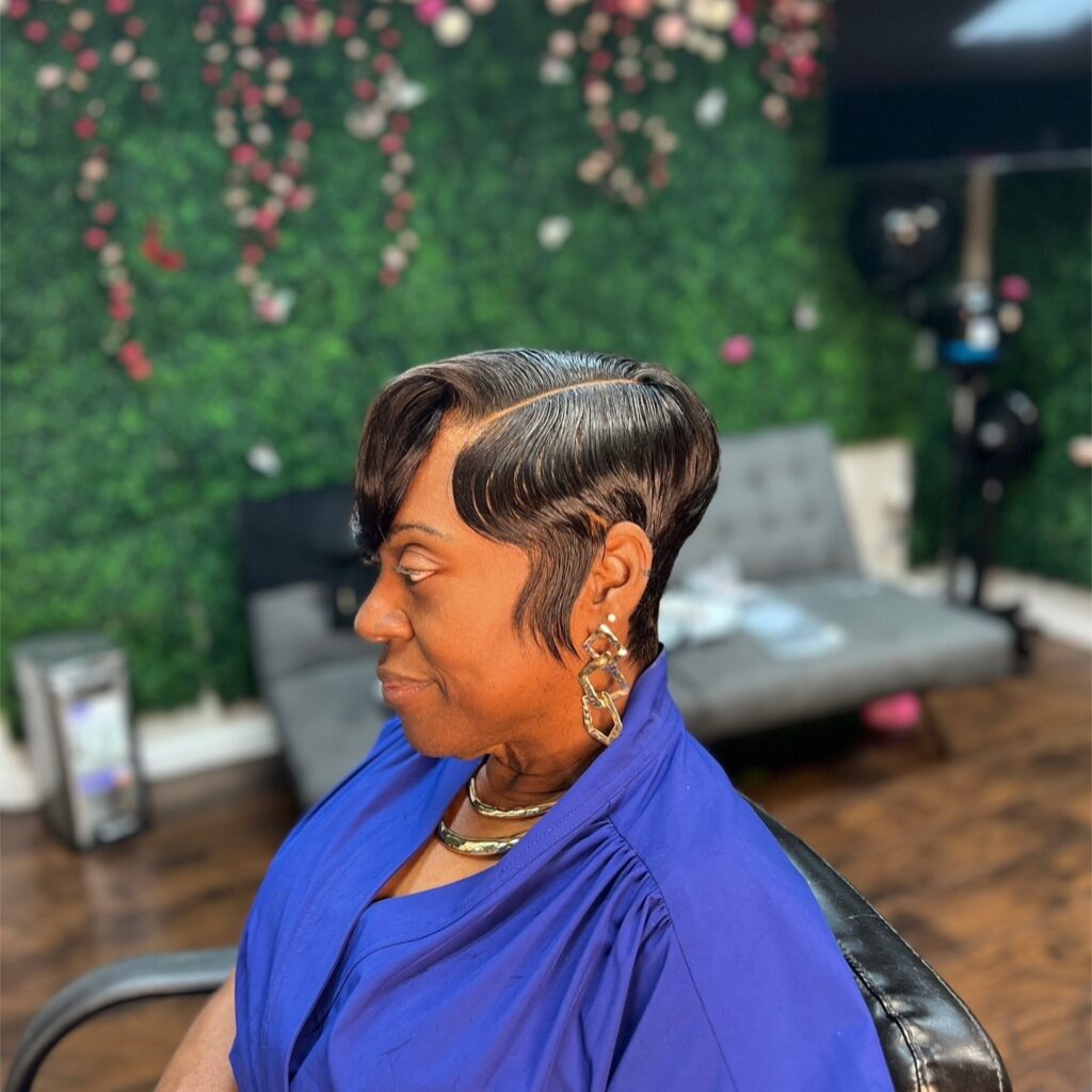 A woman with a sleek dark pixie haircut featuring sculpted finger waves and a precise side part.