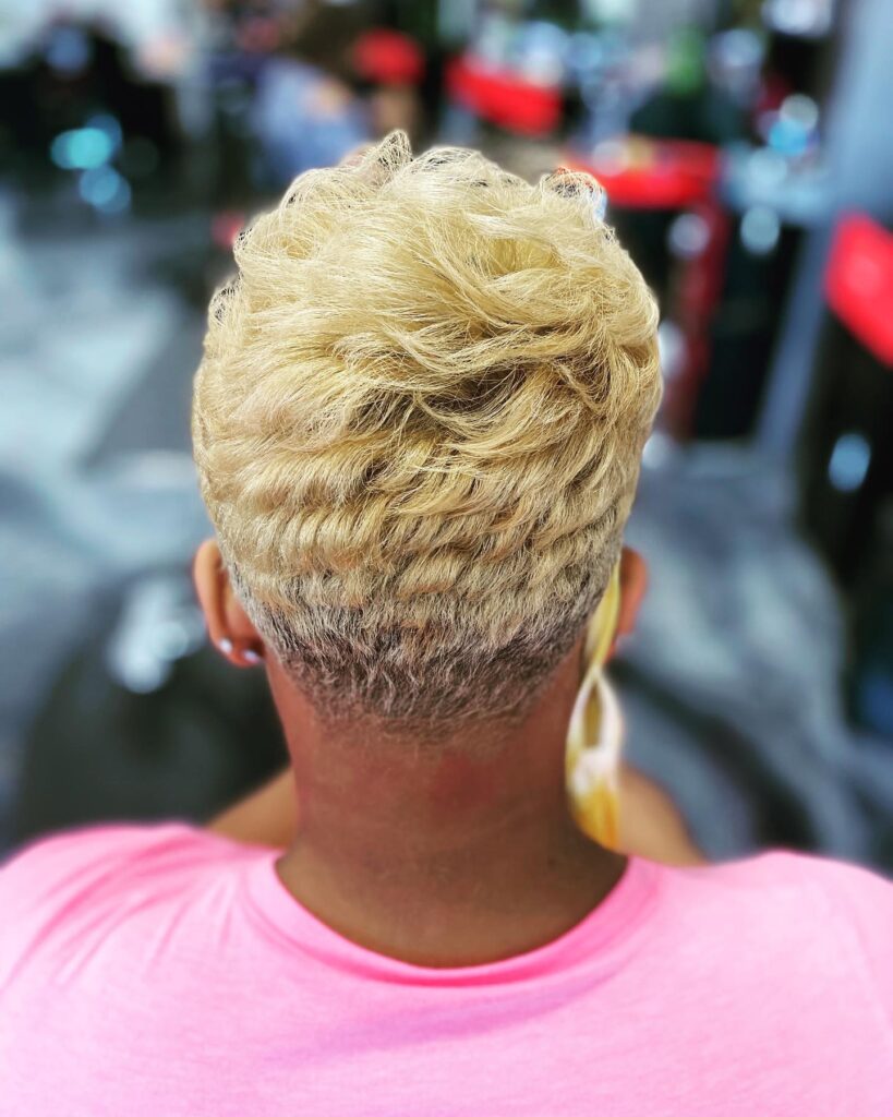 A back view of a woman with a honey blonde tapered haircut featuring textured waves on top. 