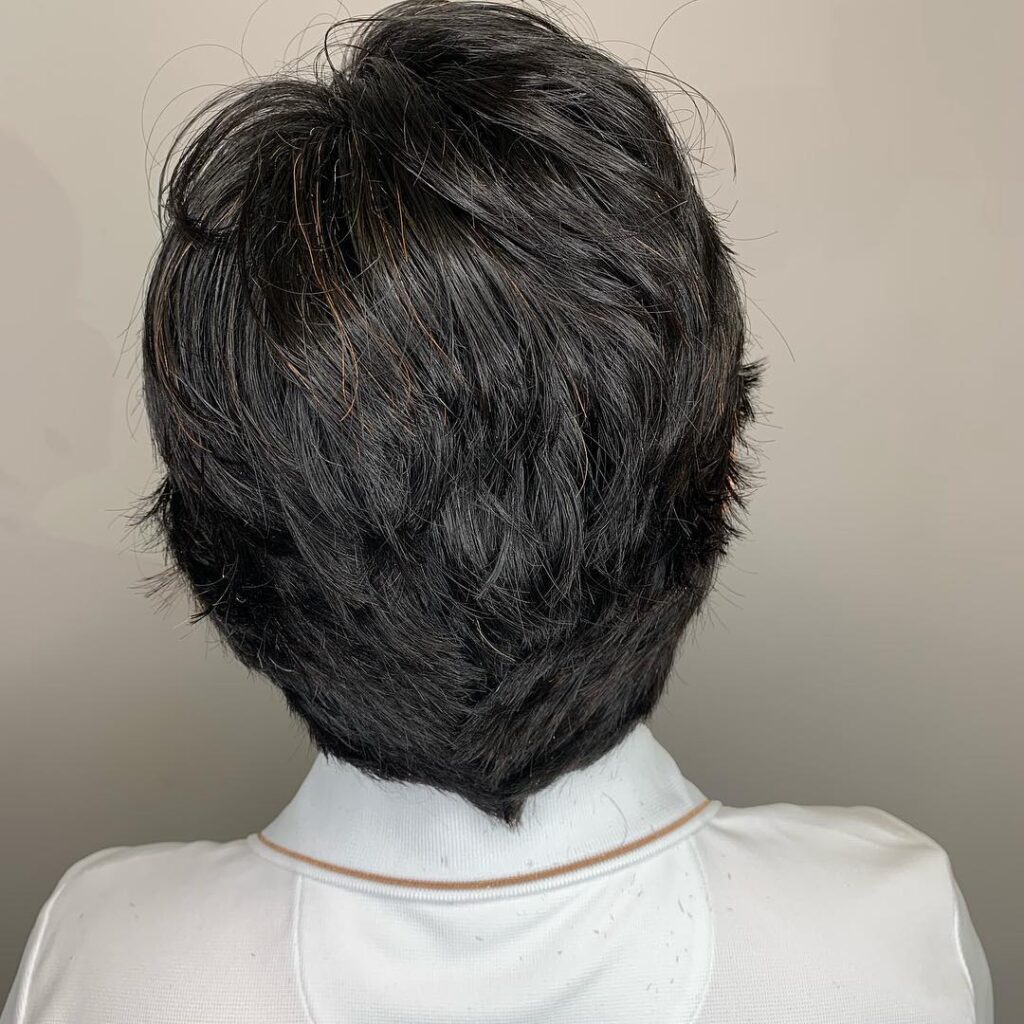 A back view of a woman with a dark textured layered inverted bob haircut featuring subtle coppery highlights.