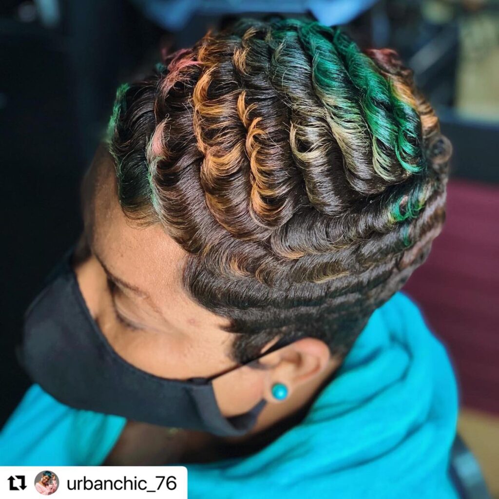 A woman with short dark hair styled in glossy finger waves with vibrant highlights in green copper and pink.