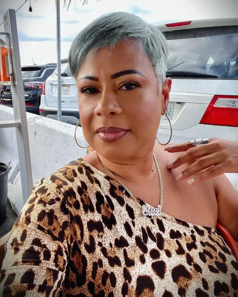 A woman wearing a textured silver pixie haircut with side swept bangs. 