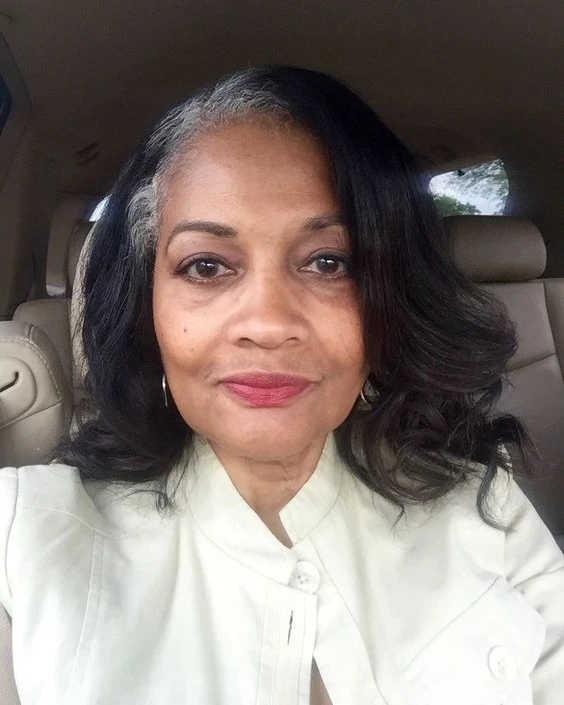 A woman with shoulder length dark curly hair featuring natural silver highlights near the temples.