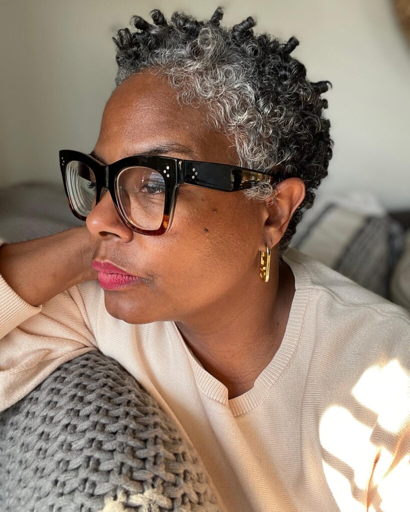 A woman with a short salt and pepper curly hairstyle featuring small defined finger coils.