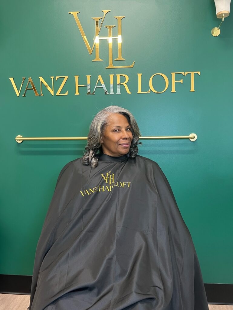 A woman with a shoulder length textured curly gray hairstyle.