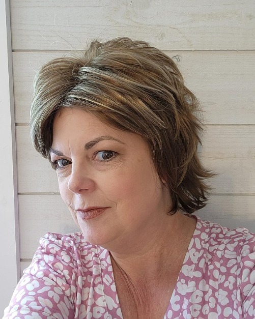 A woman with an oval face shape wears a tousled honey brown shag hairstyle with golden highlights and feathered layers.