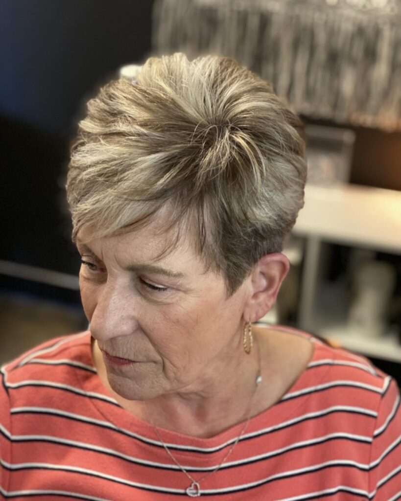 A woman with an oval face wears a professionally styled ash brown pixie cut with soft highlights and a tapered back.