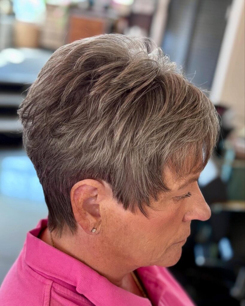 A woman with a short textured pixie haircut featuring ash brown and grey tones with feathered layers and soft bangs.