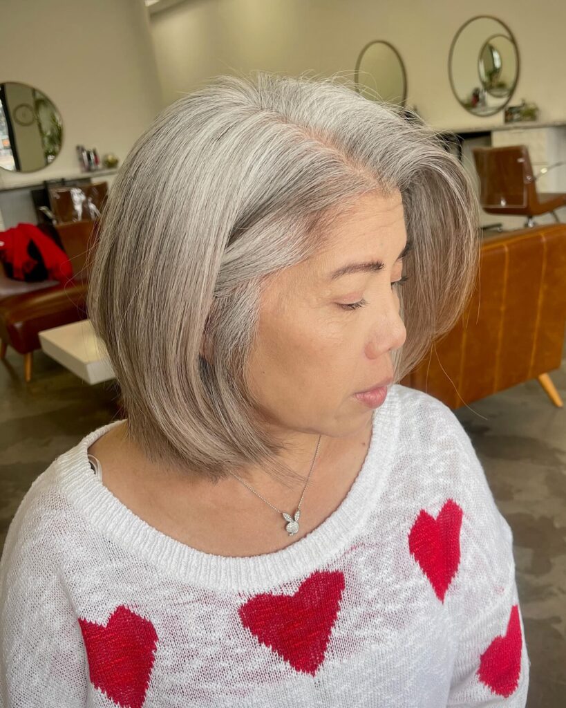 A woman with a sleek chin length silver bob featuring a deep side part and soft straight layers.