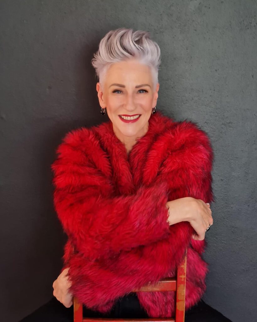 A smiling woman with a short silver undercut hairstyle featuring a voluminous brushed back top.