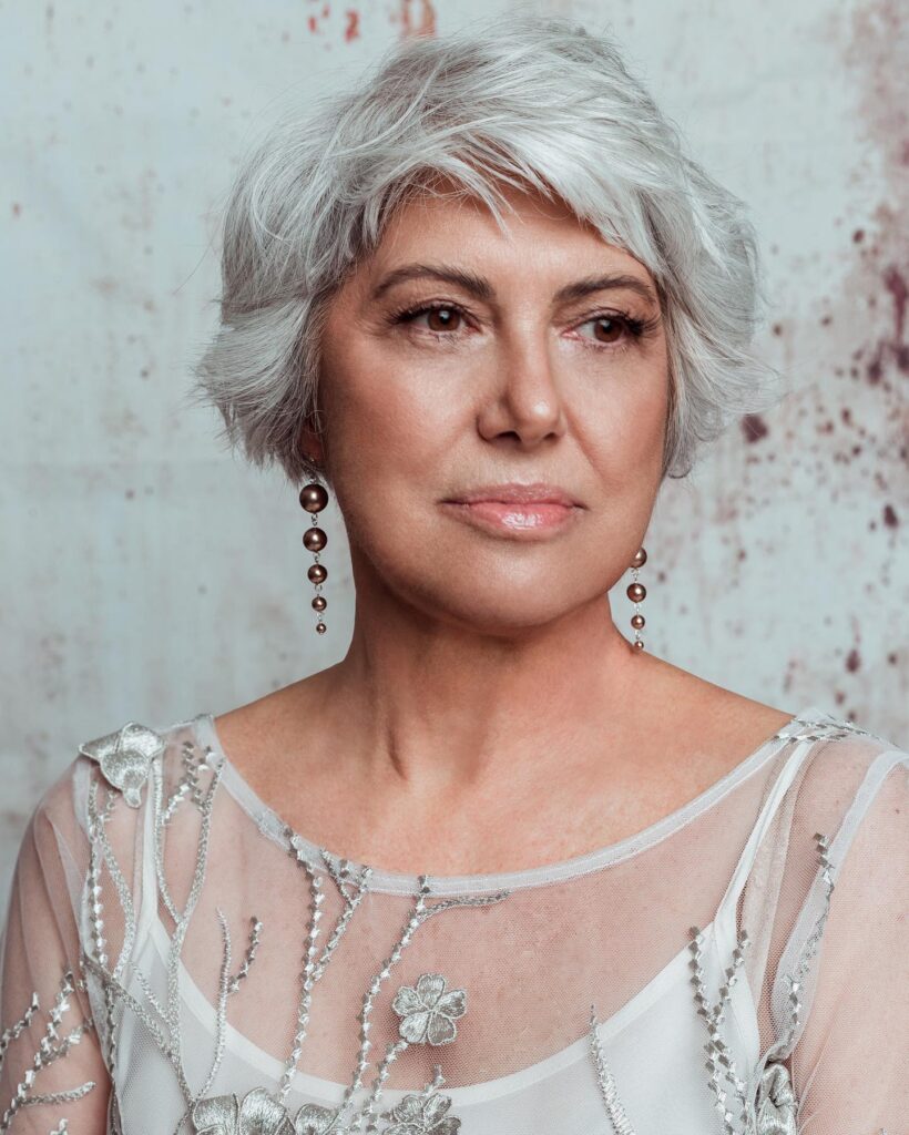 A woman with a voluminous silver shaggy hairstyle featuring feathered layers and wispy bangs.