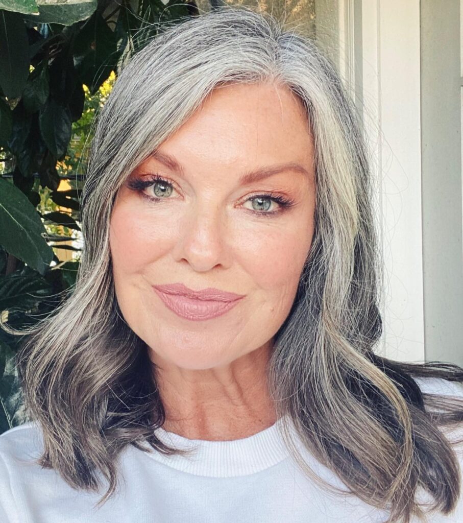 A woman with shoulder length wavy hair in a multidimensional silver and grey color with a side part.