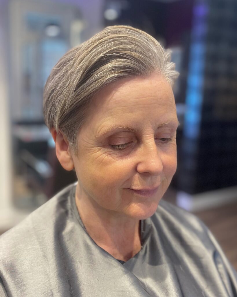 A woman with a very short and smooth silver pixie cut styled away from the forehead.