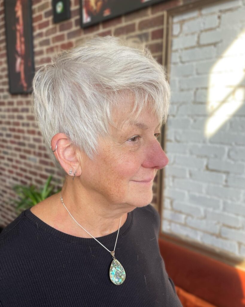 A woman with a short textured silver pixie haircut featuring layers and height at the crown.