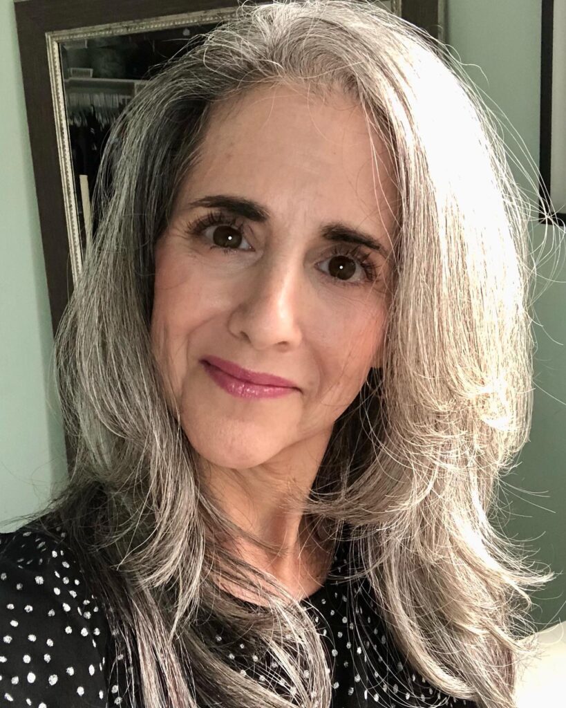 A woman with long layered silver and grey hair that has feathered ends and face framing pieces.