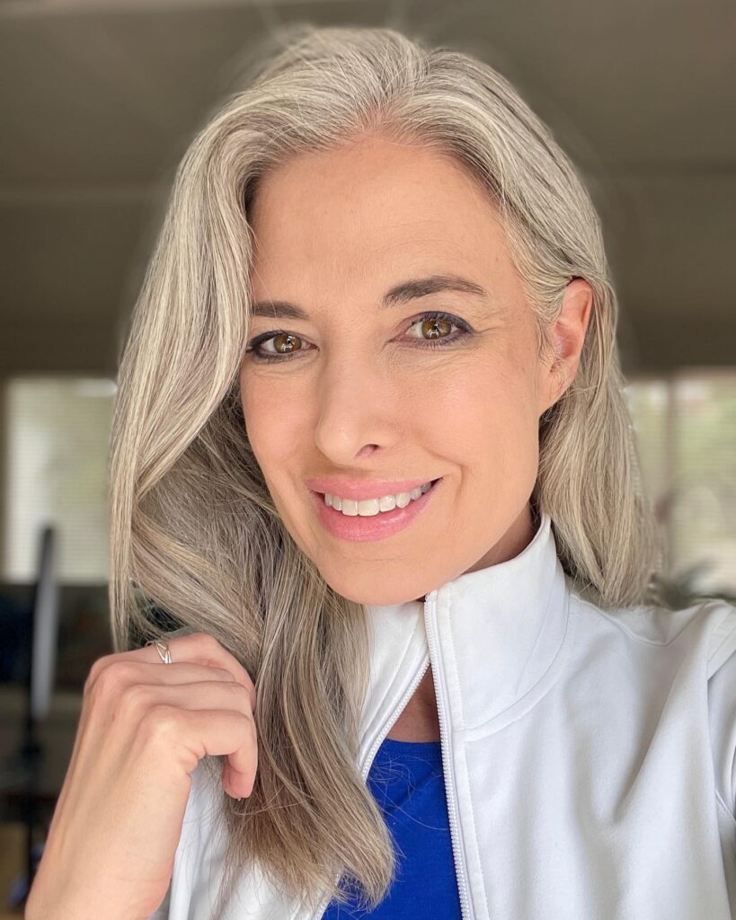 A woman with long silky silver hair styled with a deep side part and soft layers.