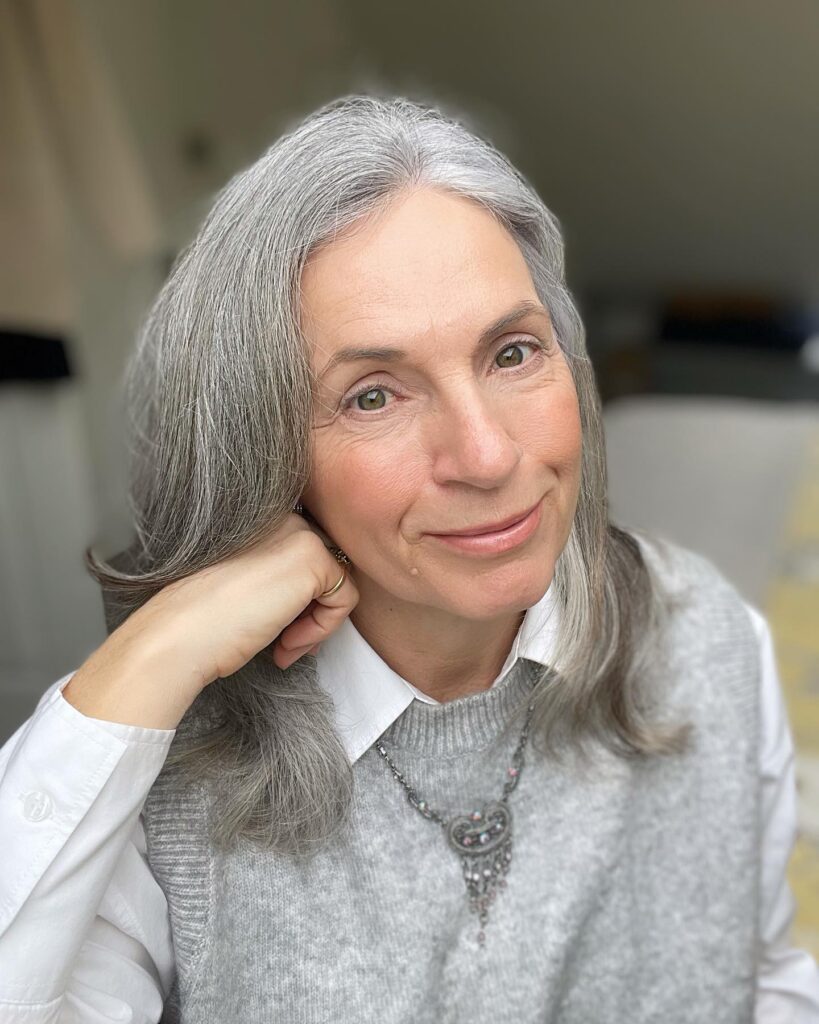 A woman with medium length straight silver hair that curves softly at the shoulders and is styled with an off center part.