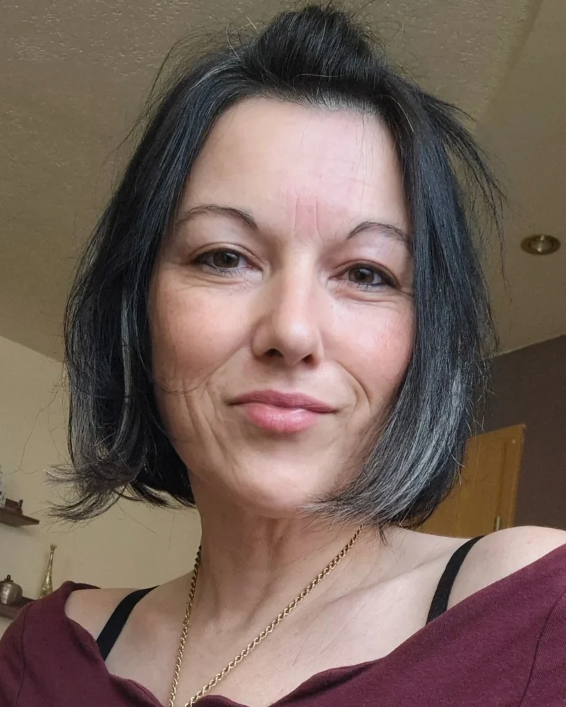 A woman with a chin length jet black bob hairstyle featuring subtle silver highlights and a smooth finish.