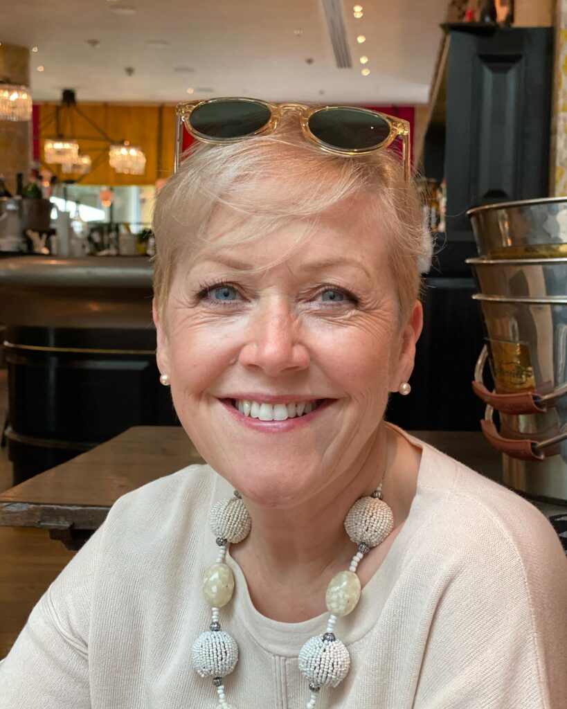 A smiling woman with a short champagne blonde pixie cut styled with a soft side swept fringe.