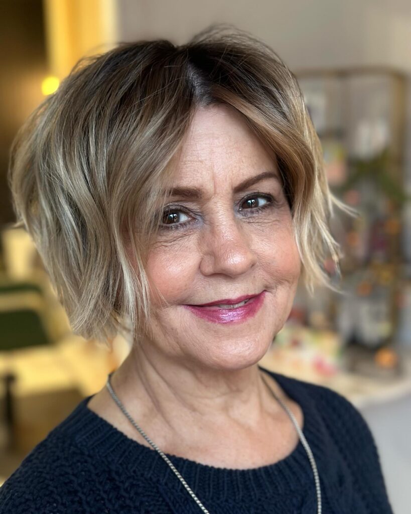 A woman with a textured honey blonde bob featuring dark roots and choppy layers styled with beachy waves.
