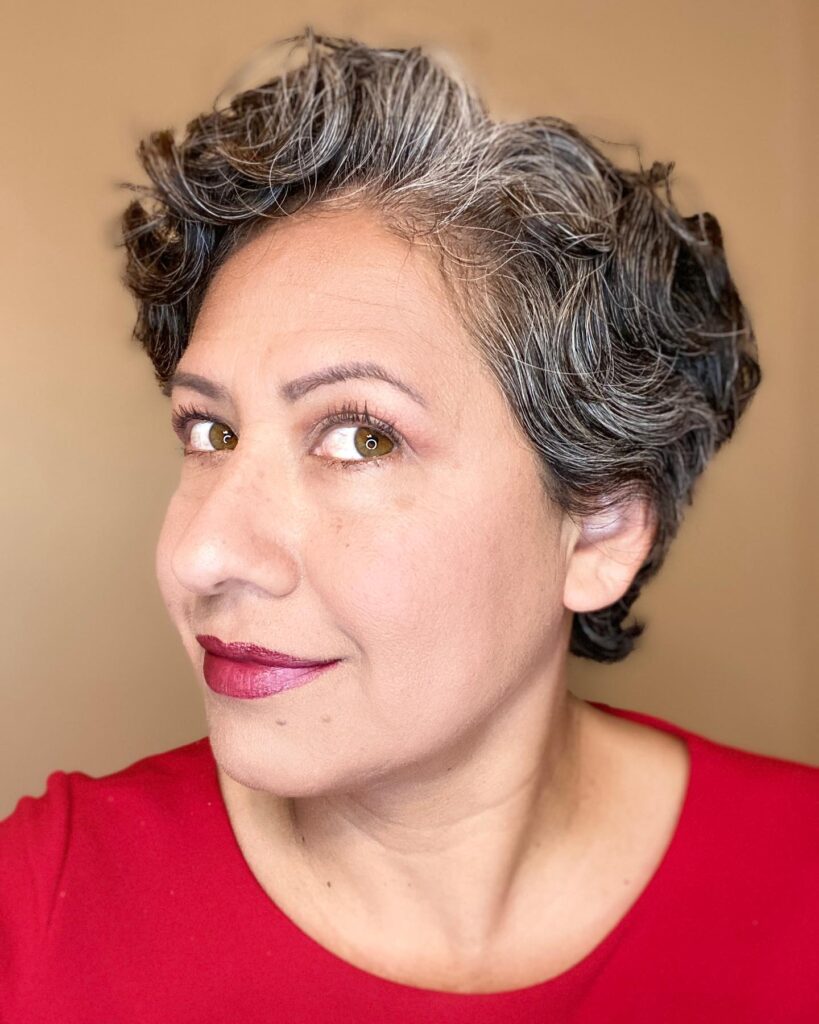 A woman with short wavy salt and pepper hair styled in a voluminous pixie cut.