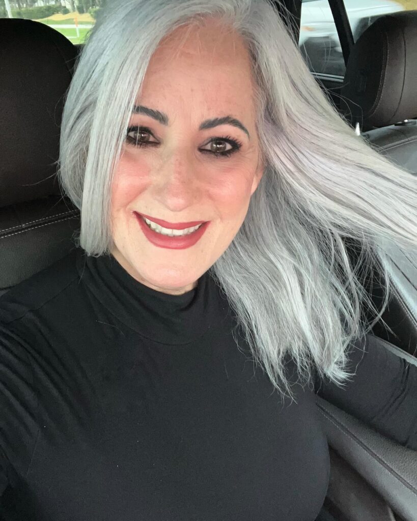 A woman with smooth mid length silver hair styled with a deep side part and subtle volume.