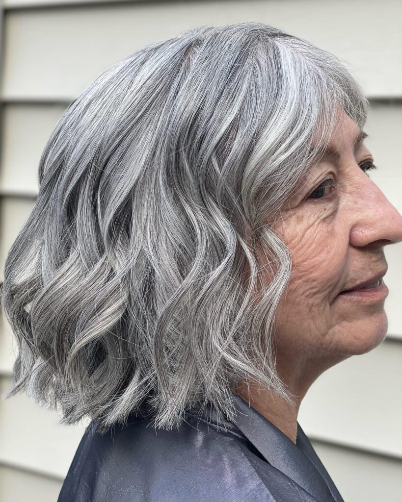A woman with natural gray and silver hair styled in a wavy shoulder-length bob with a side part.