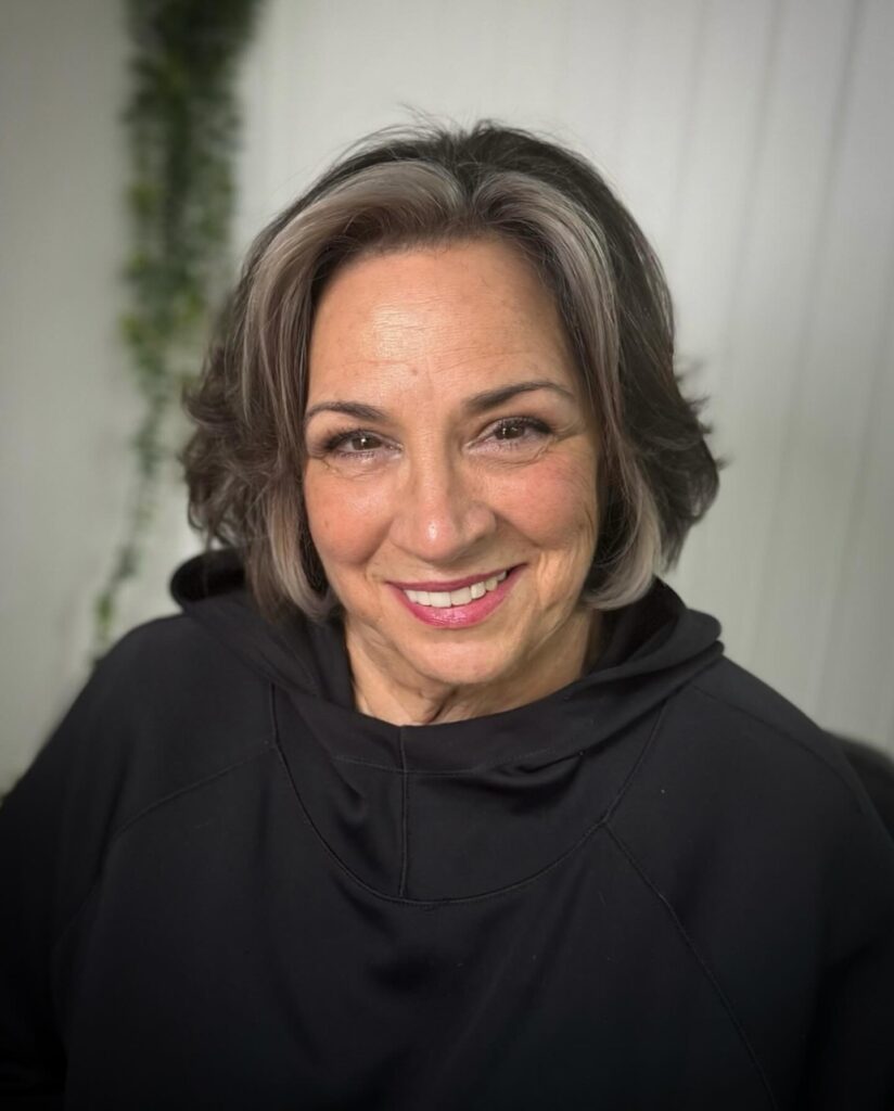 A woman with a voluminous chin length ash brown bob featuring bright silver face framing highlights.