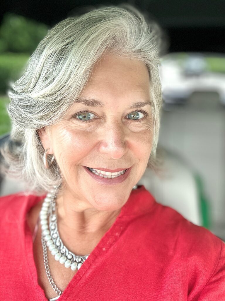 A woman with a sleek chin length silver bob featuring a dramatic side swept fringe and a deep side part.