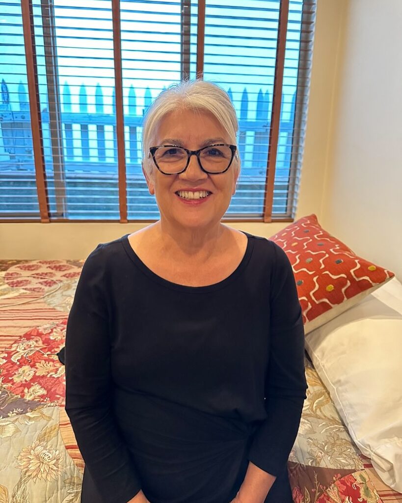 A smiling woman with glasses wearing her natural silver hair in a sleek pulled back updo with a center part.