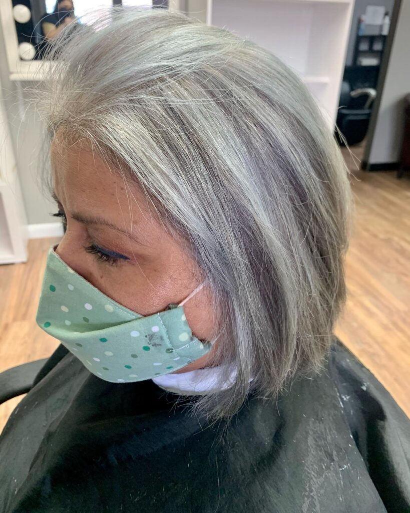 A woman with a chin length bob in a bright natural silver color styled with a gentle swept back volume at the roots.