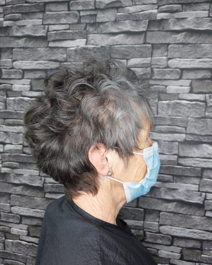 A woman with a short tapered pixie haircut featuring natural charcoal grey curls and a textured voluminous top.