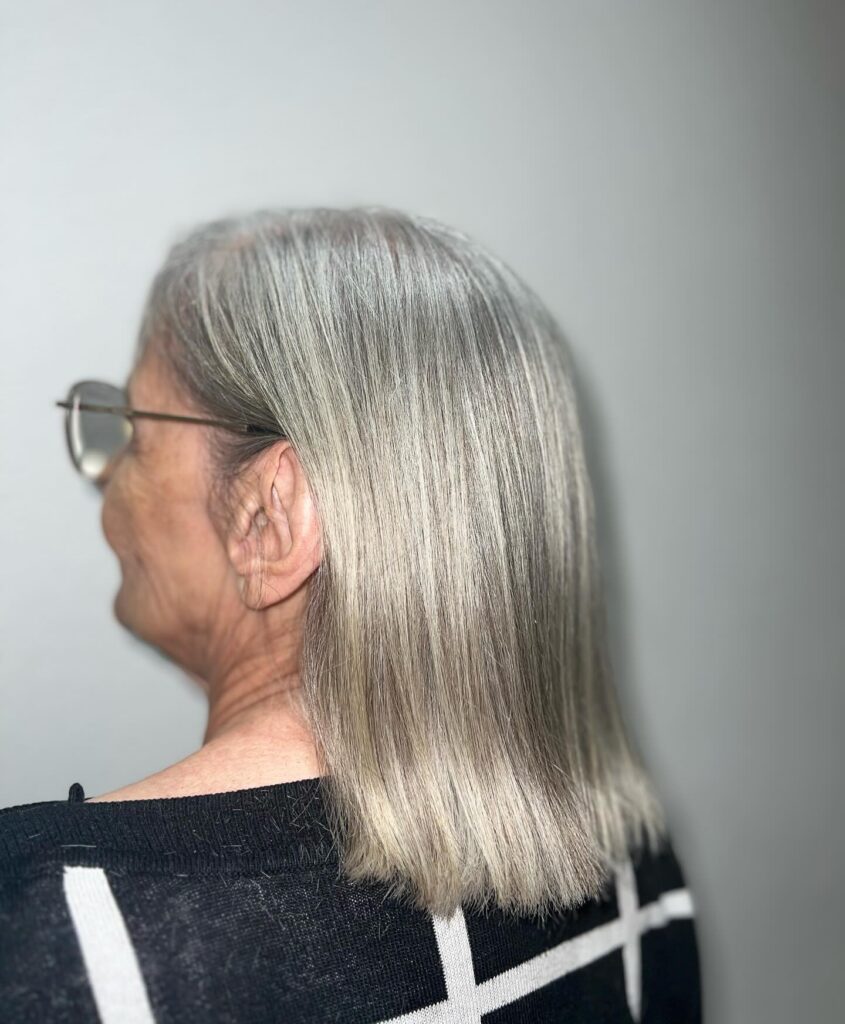 A woman with straight shoulder length hair in a natural ash grey shade featuring a blunt horizontal cut.