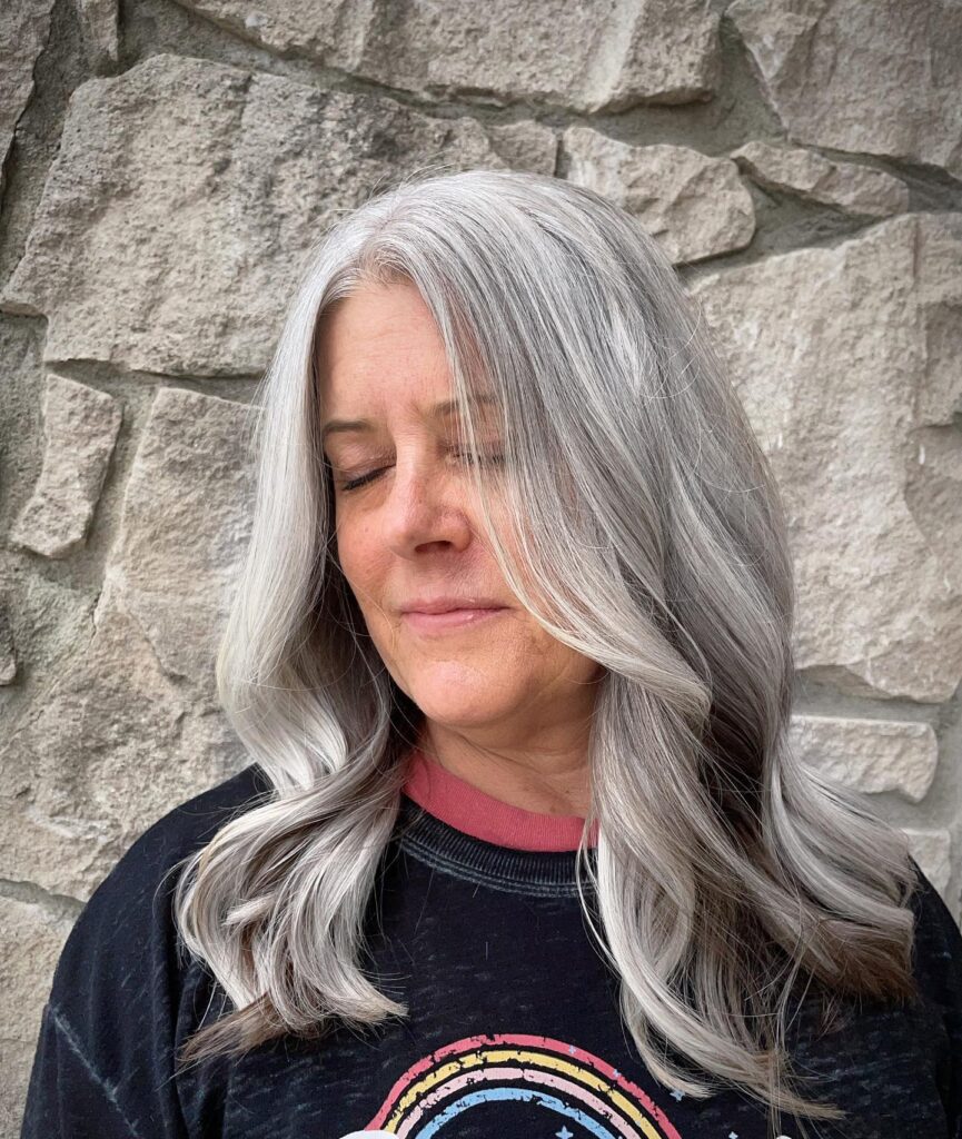 A woman with medium length silver hair styled in soft flowing waves with a slight side part.