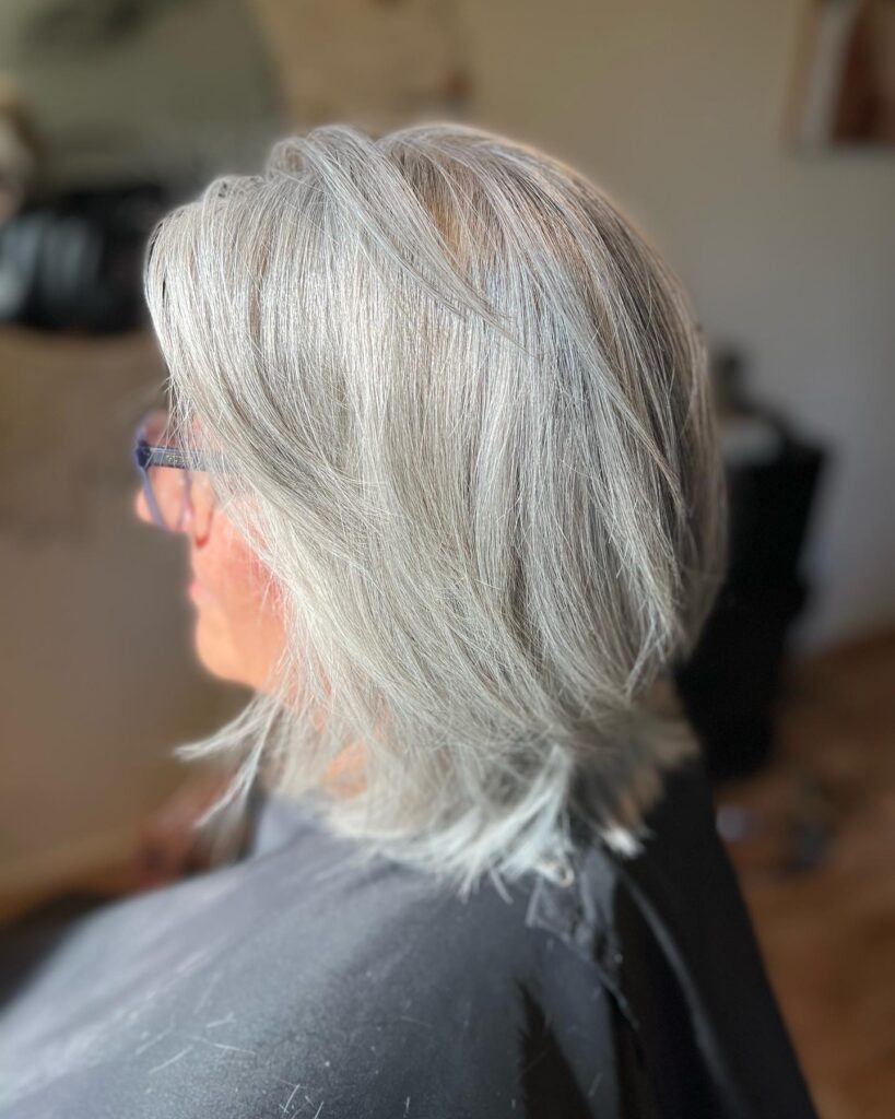A woman showing a shoulder length straight haircut in a bright natural silver color with soft layered ends.