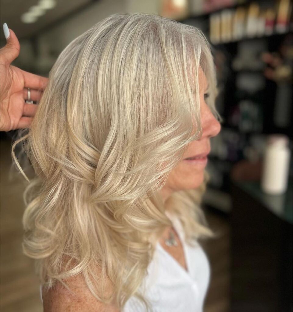 A woman with medium length layered champagne blonde and silver hair styled in soft voluminous waves that frame her face.
