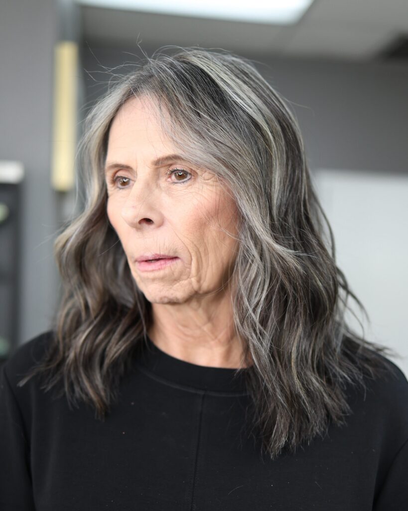 A woman with shoulder length salt and pepper hair styled in natural loose waves with a middle part.