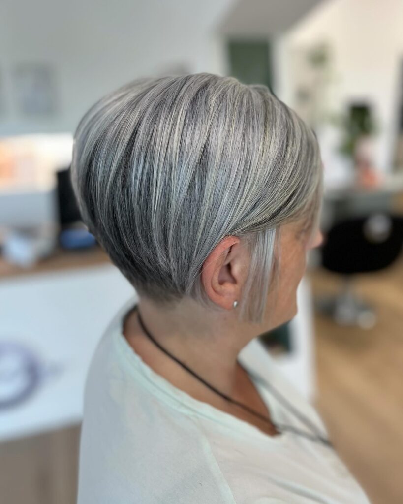 A woman with a sleek salt and pepper tapered pixie cut featuring smooth layers and a clean neckline.