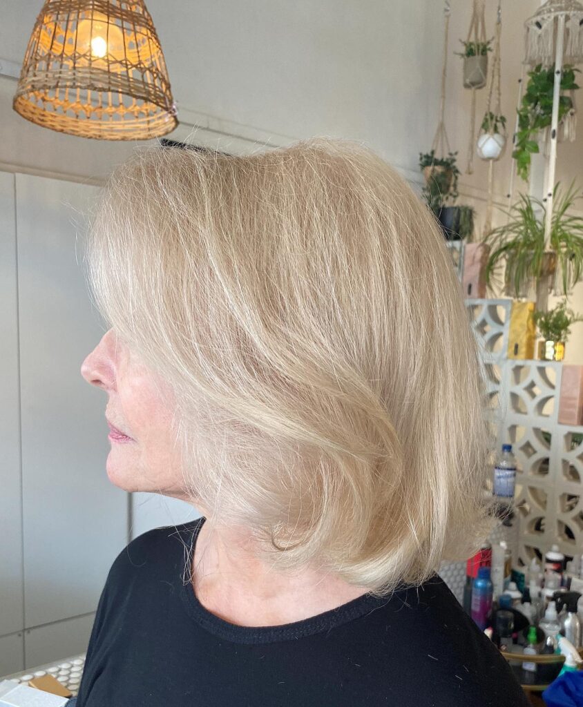 A woman with a neck length layered bob in a soft sand blonde shade featuring a gentle side sweep.
