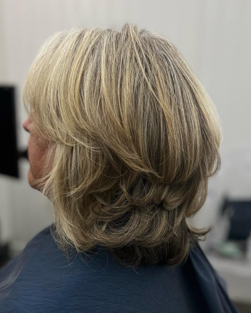 A woman with a heavily layered neck length bob featuring golden blonde and deep lowlights viewed from the side.