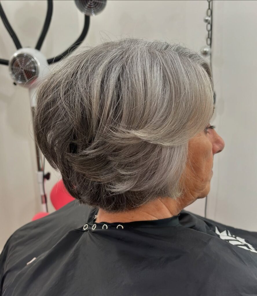 A woman with thick silver and grey hair styled in a layered feathered bob with a tapered neckline.