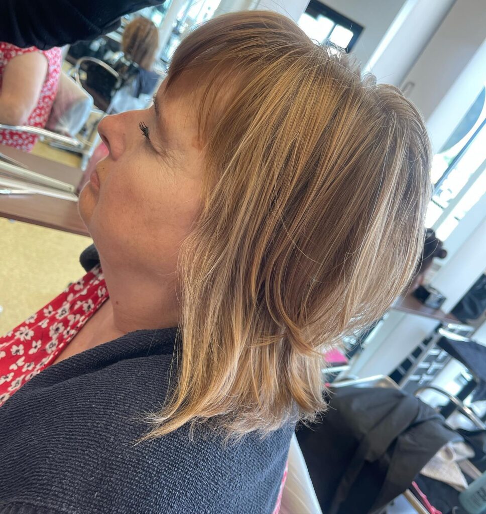 A woman with shoulder length sandy blonde hair featuring golden highlights and a soft wispy fringe.