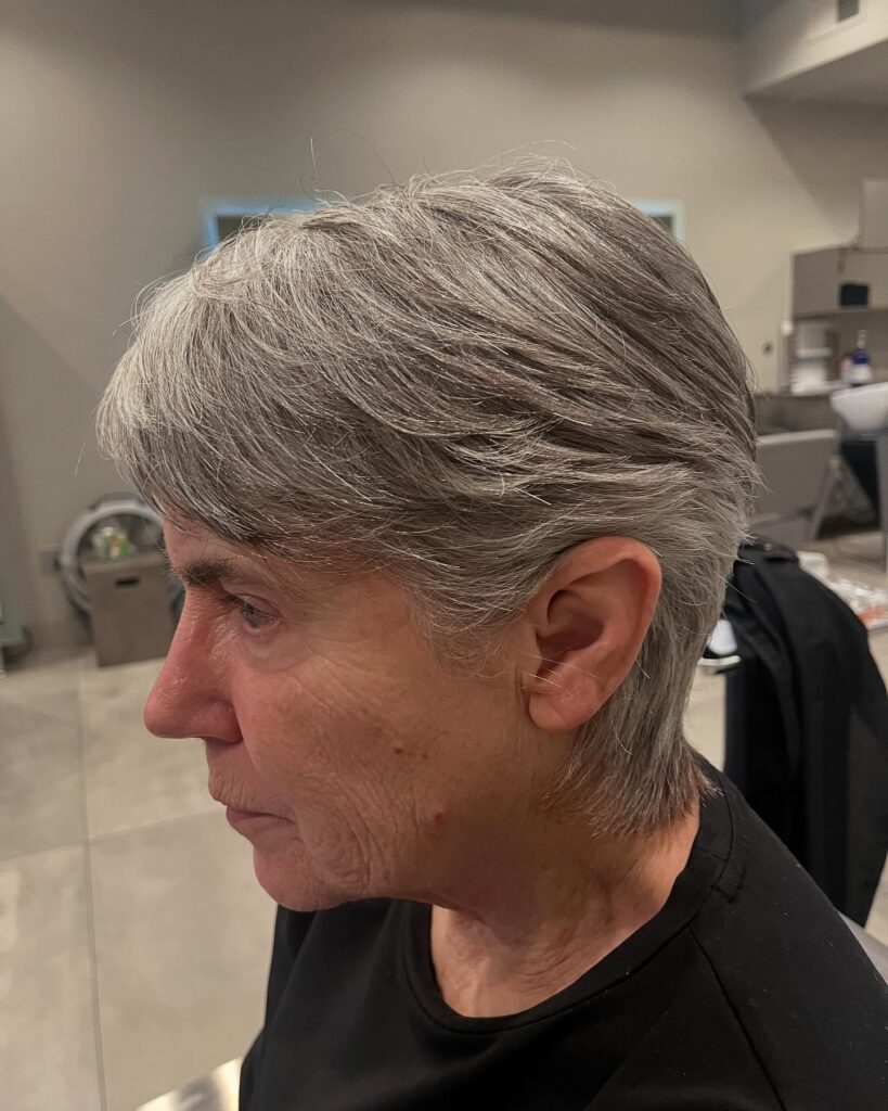 A woman with short pewter grey hair in a layered pixie cut brushed back from her face and tapered at the neck.