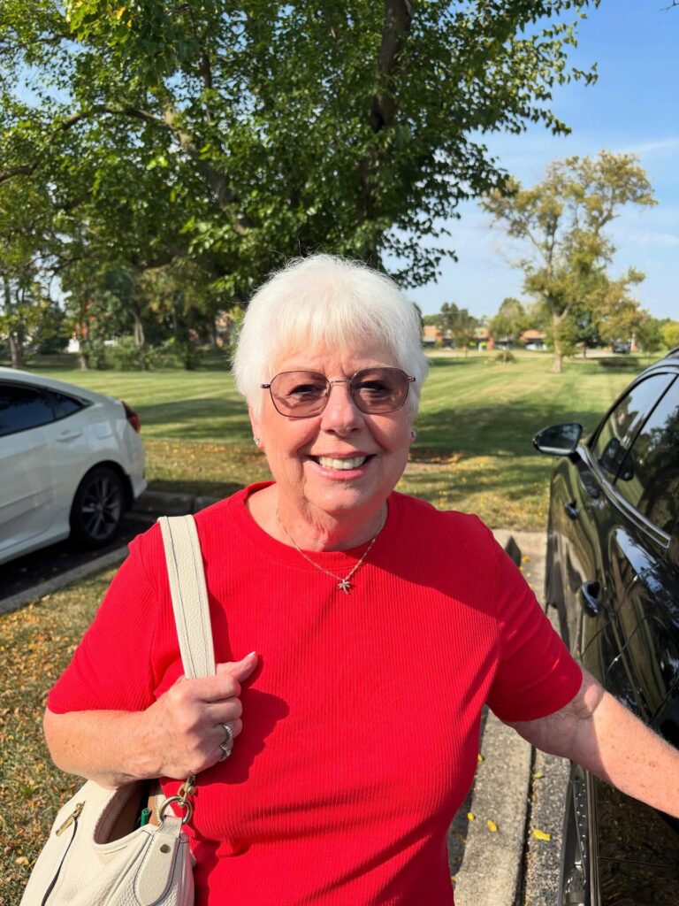 A smiling woman in a red shirt wearing a bright white short pixie cut with full textured bangs.
