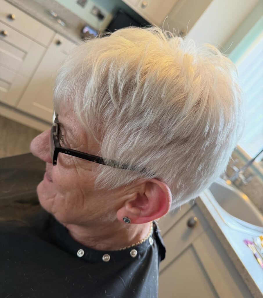 A woman with thick white hair in a short wispy pixie cut with tapered sides and a textured top.