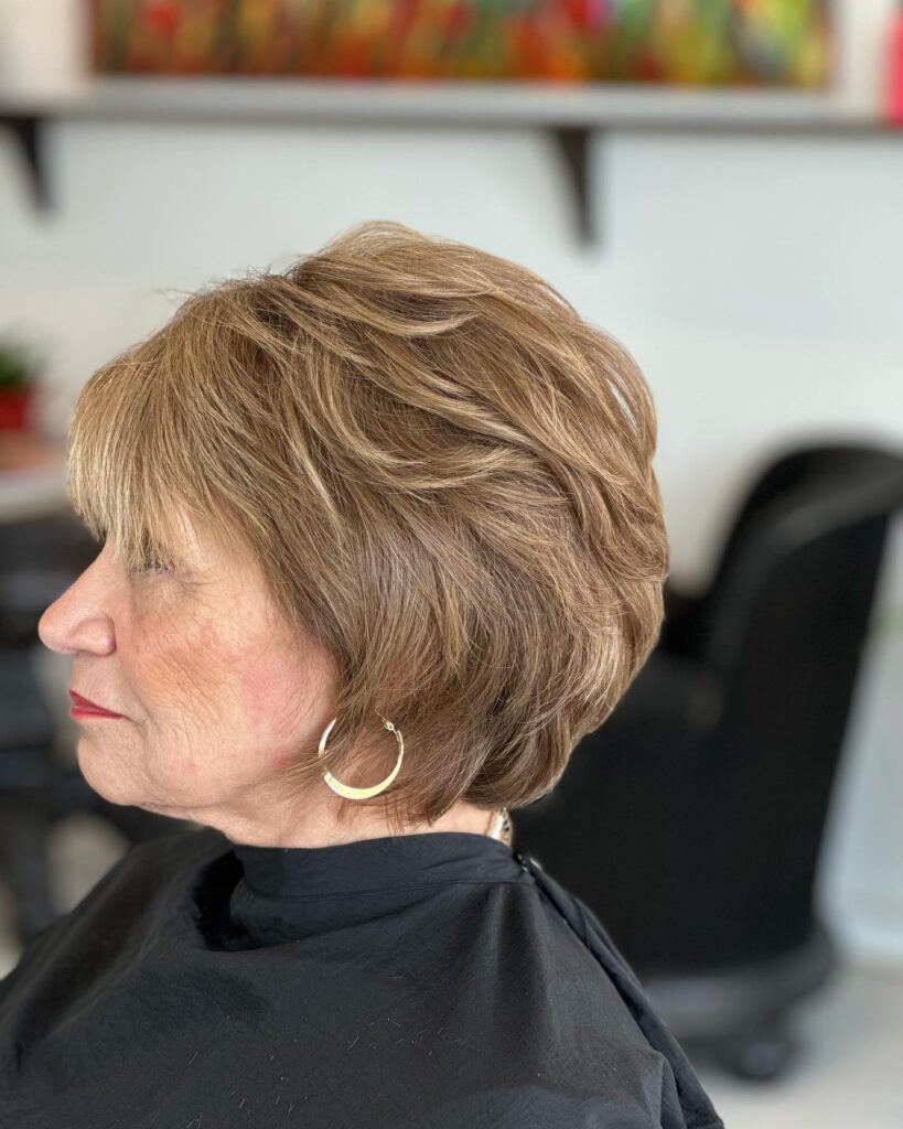 A woman with thick light honey brown hair in a neck length voluminous layered bob with a soft fringe.