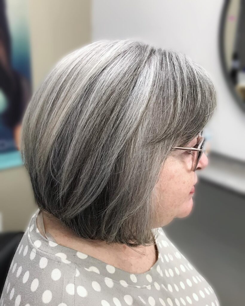 A woman viewed from the side showcasing a short stacked bob in a multi tonal silver and grey color with side swept bangs.