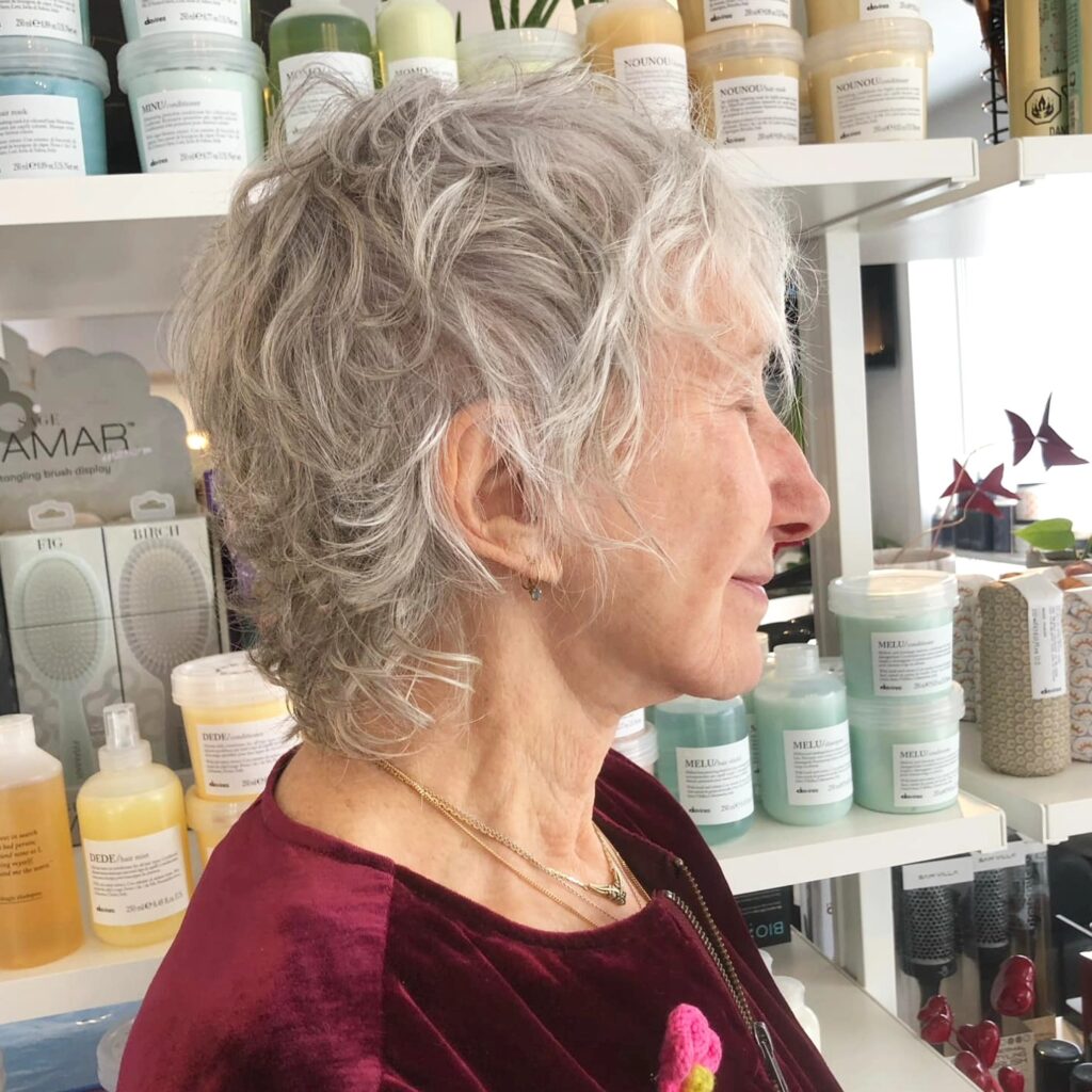 A woman with thick silver hair styled in a wavy shaggy cut with textured layers and a piecey finish.