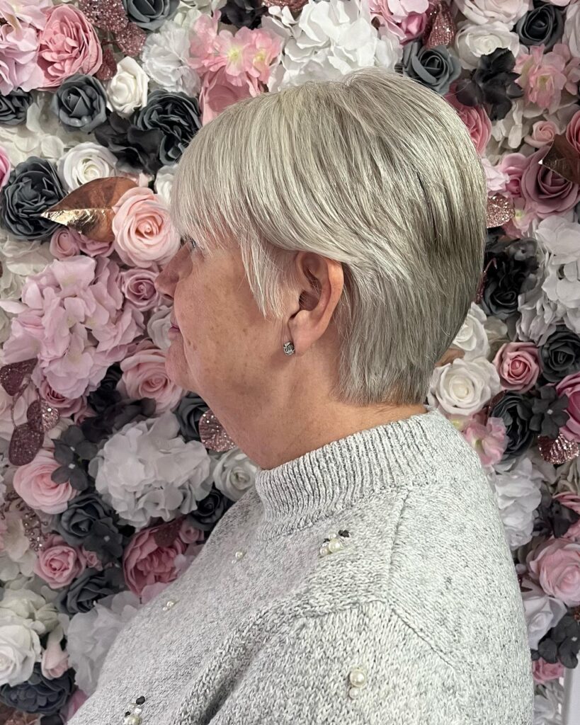 A woman with thick straight silver hair styled in a sleek bowl cut pixie with a full fringe.