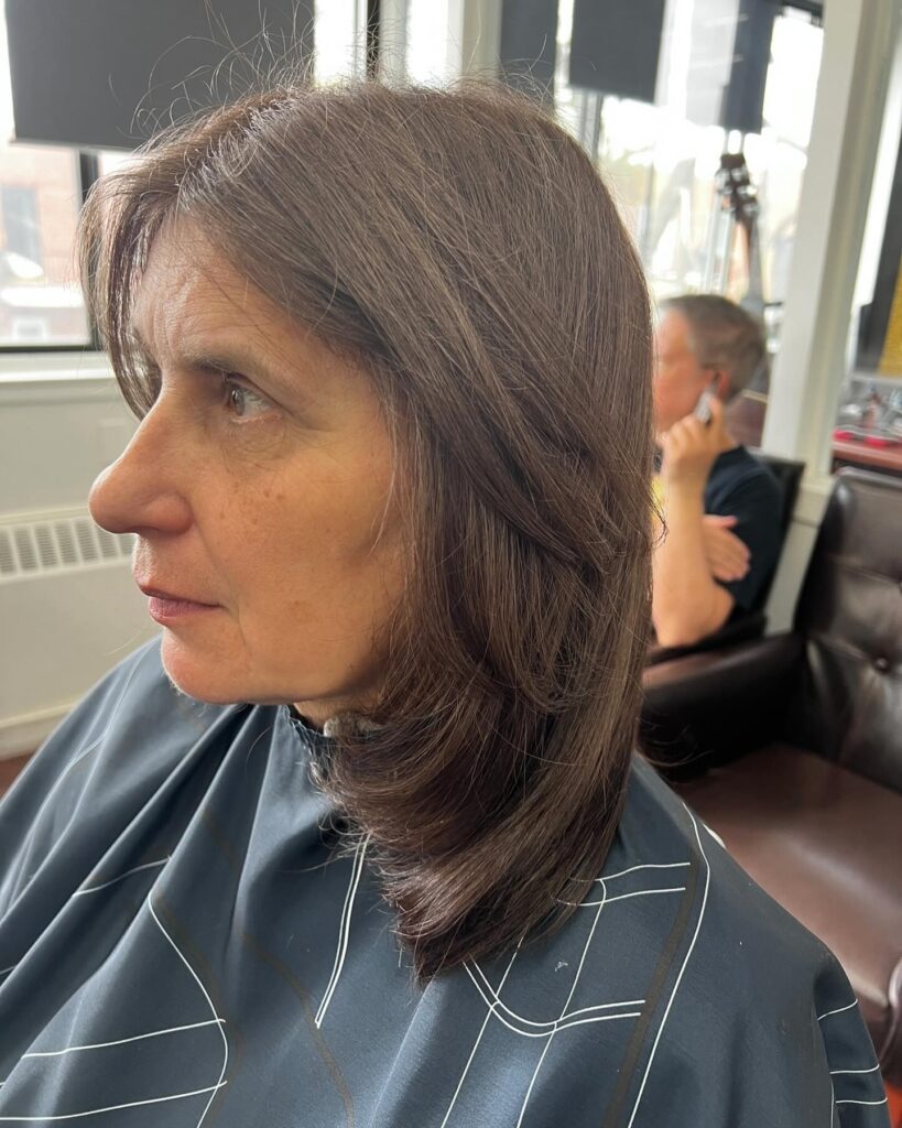 A woman with thick ash brown hair styled in a straight mid length cut with soft face framing layers.